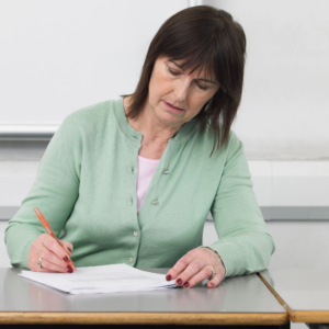 A teacher marking a book at a desk.